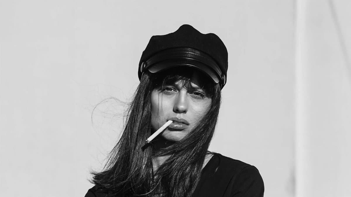Black and white portrait of a woman in a hat smoking a cigarette, depicting solitude and contemplation.