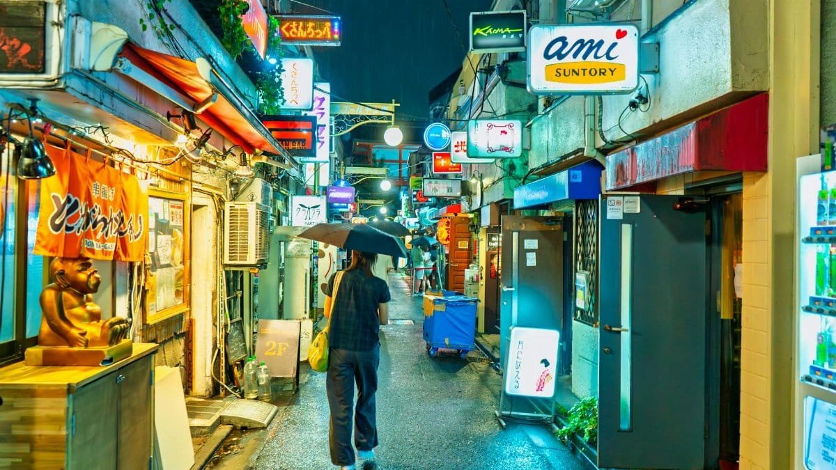Colorful Tokyo alleyway at night with bright signs and a person holding an umbrella.