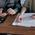 A couple diligently reviews their finances using a calculator and documents at home.