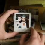 Close-up of hands holding a nostalgic Polaroid photo of father and son from a memory box.