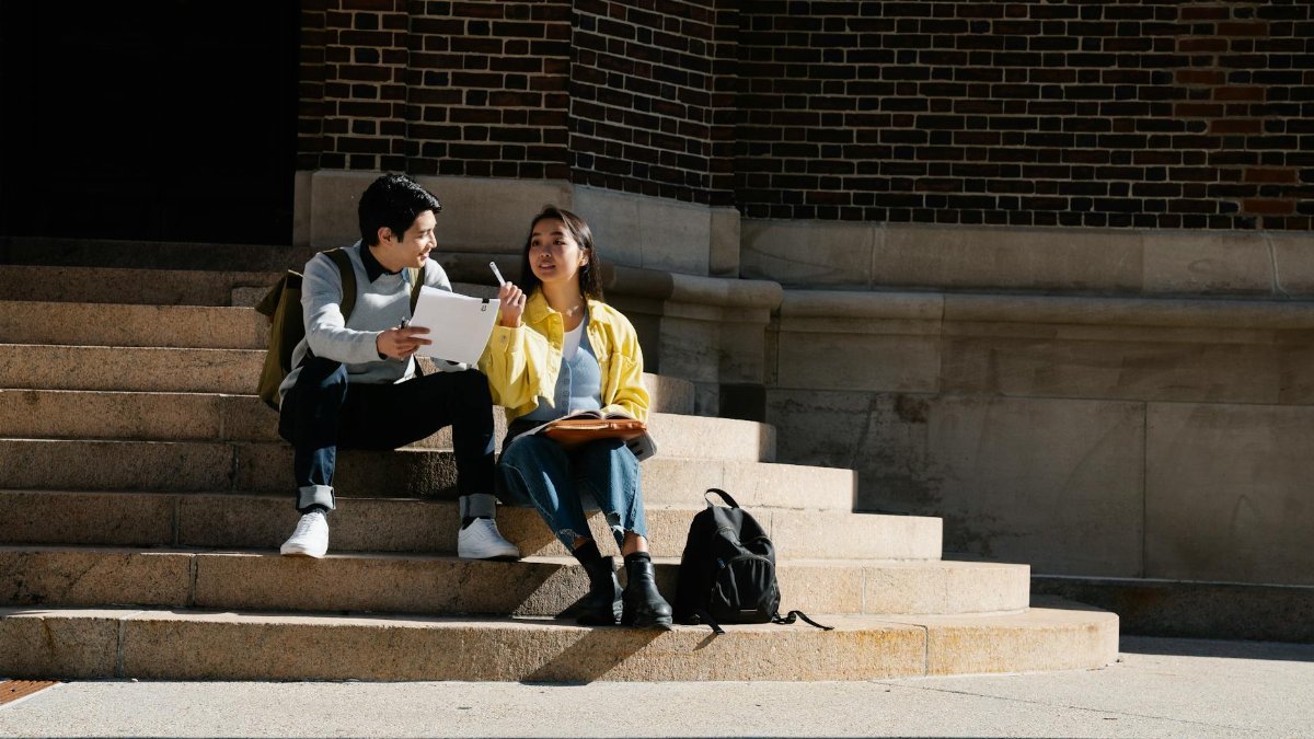 Two college students sitting on steps outdoors studying together in natural light.