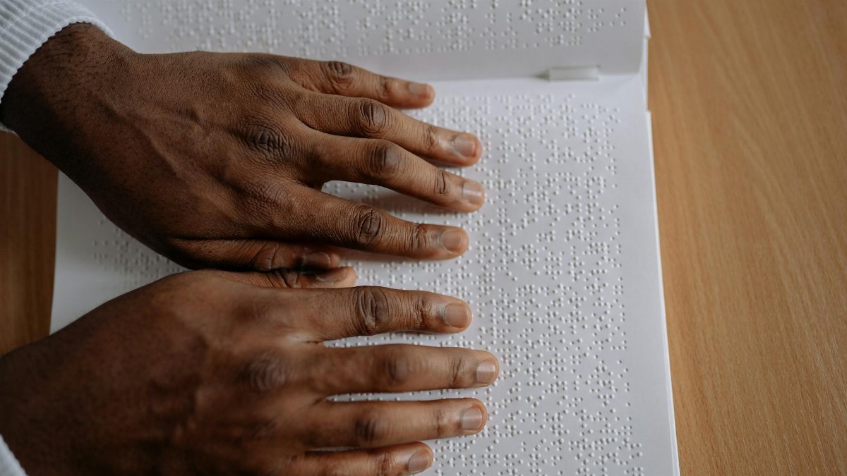 A close-up view of hands reading an open book with Braille alphabet.