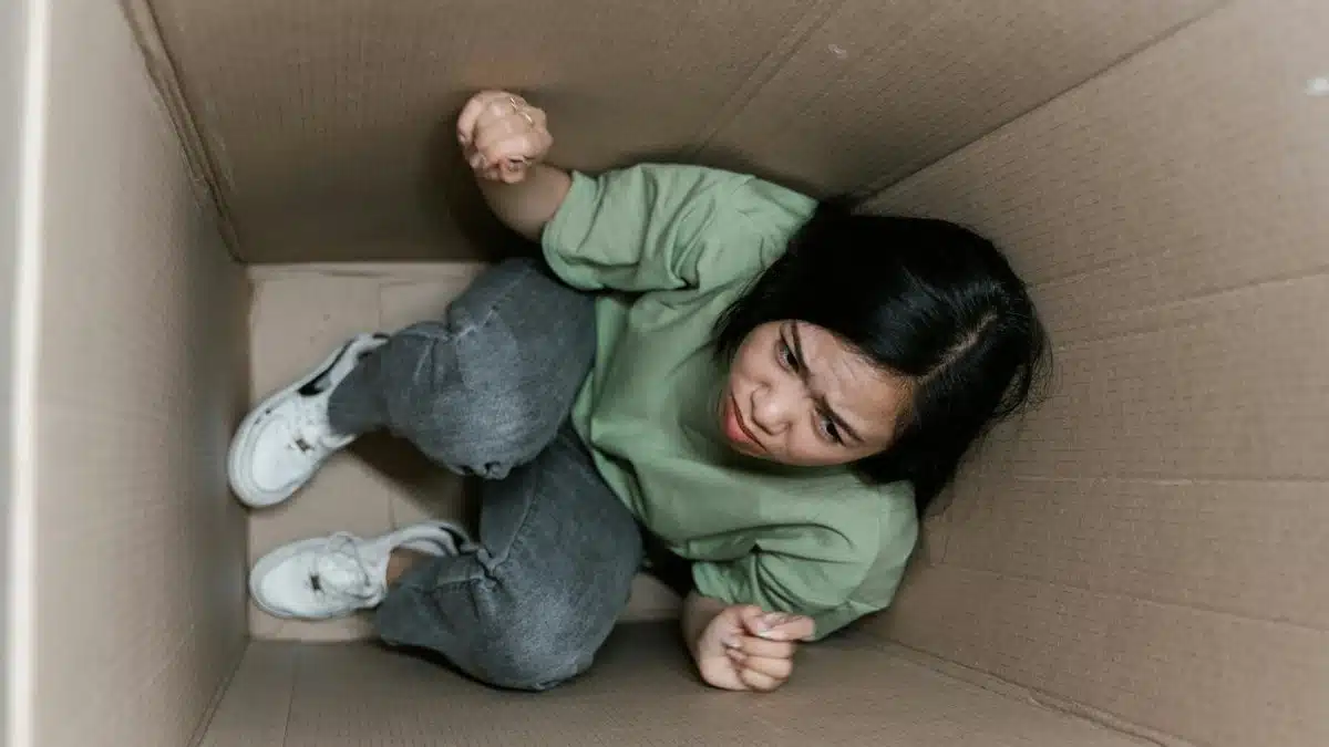 A woman feeling trapped and anxious inside a small cardboard box, symbolizing claustrophobia.