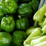 Close-up of fresh green bell peppers and chili peppers, showcasing vibrant and organic produce in a market setting.