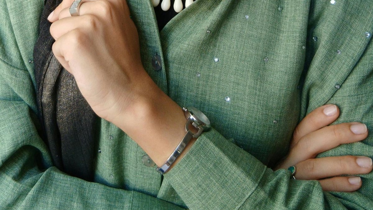 Close-up of a person in a green outfit accessorized with a necklace and watch, showcasing chic style.