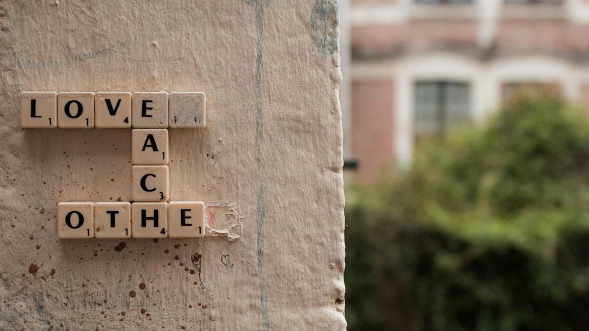 Scrabble tiles spelling 'Love Each Other' on a textured wall in Lille, France.