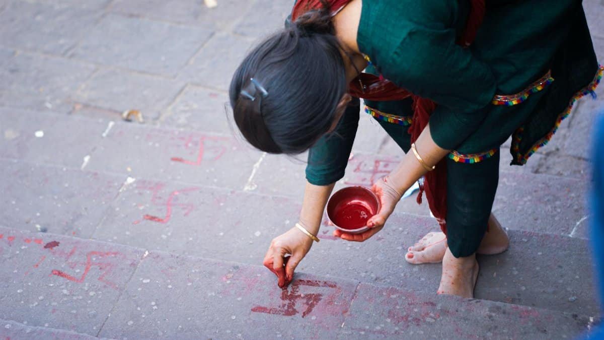 A woman creating traditional rangoli designs on steps using red powder in Pavagad, India.