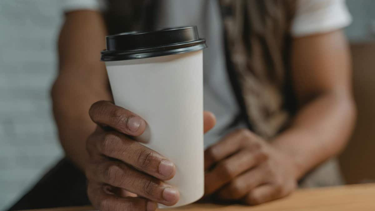 Hand holding a white disposable takeaway coffee cup with black lid, close-up view.