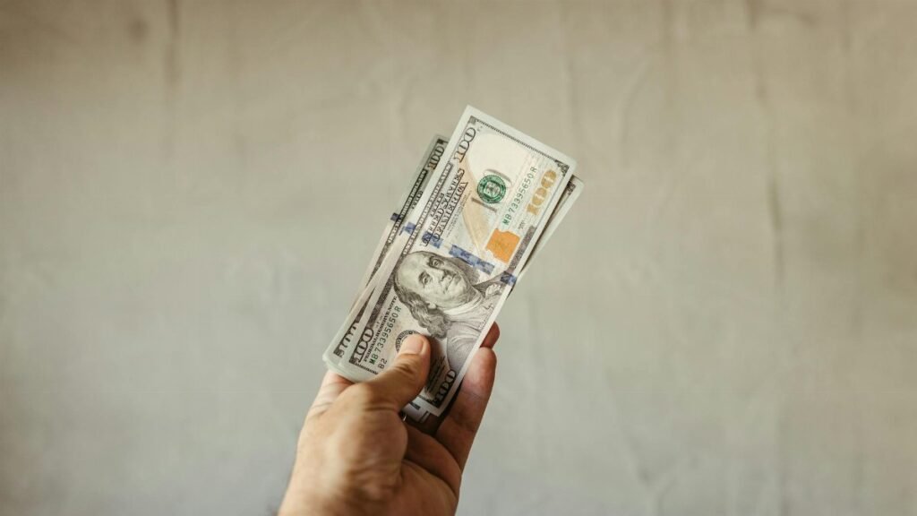A hand holding a stack of US dollar banknotes against a neutral backdrop, symbolizing wealth.