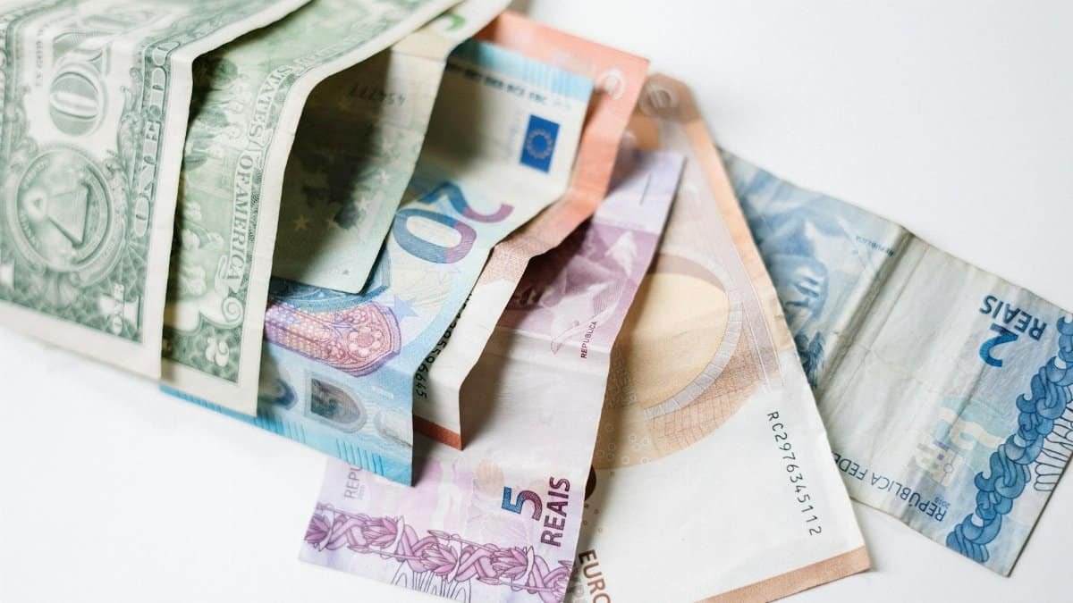 A collection of different international currency notes, including US Dollar, Euro, and Brazilian Real, on a white background.