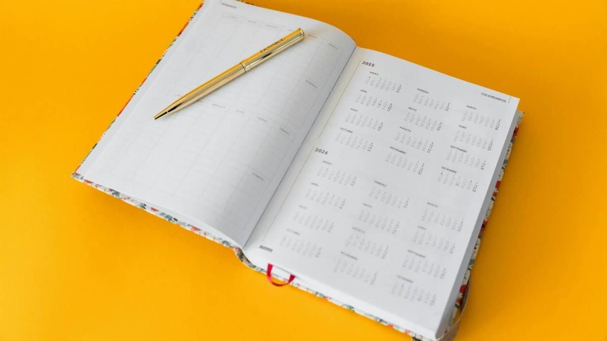 Open planner for 2023-2025 with a golden pen on a vibrant yellow background, perfect for organizing and planning.