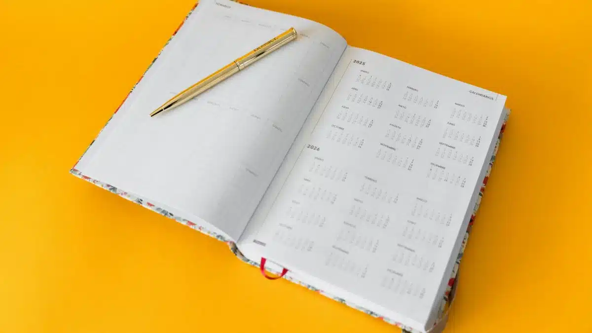 Open planner for 2023-2025 with a golden pen on a vibrant yellow background, perfect for organizing and planning.