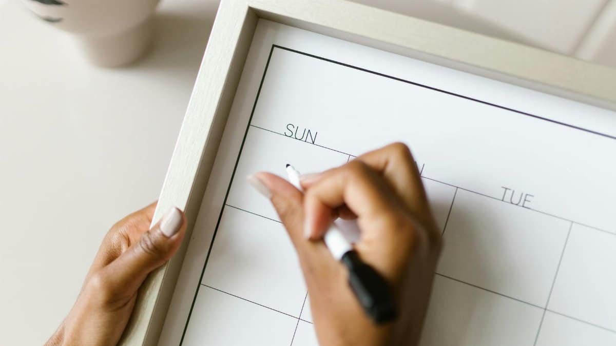 Hands holding a wall calendar, writing with a marker, organizing schedule.