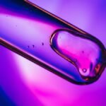 Close-up of liquid in a test tube against a vibrant purple and blue backdrop.