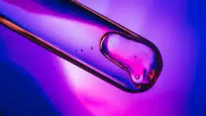 Close-up of liquid in a test tube against a vibrant purple and blue backdrop.