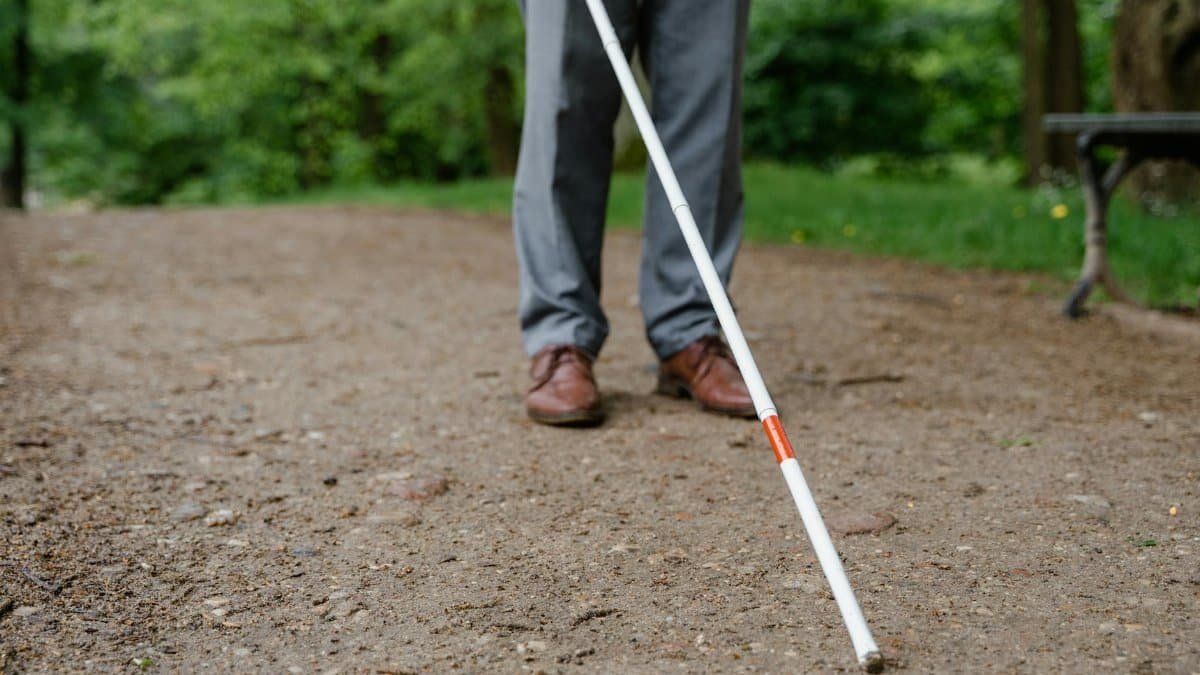 An individual with a white cane walking on a path, symbolizing independence and mobility.