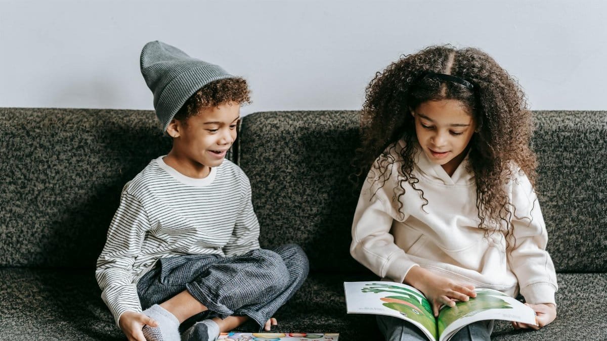 Siblings reading a picture book together indoors, fostering a love of literature.