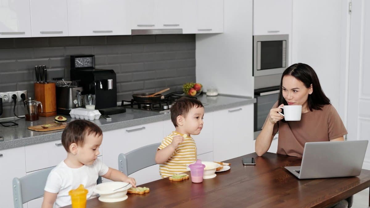 Mother and two sons enjoying breakfast while using a laptop in a contemporary kitchen.