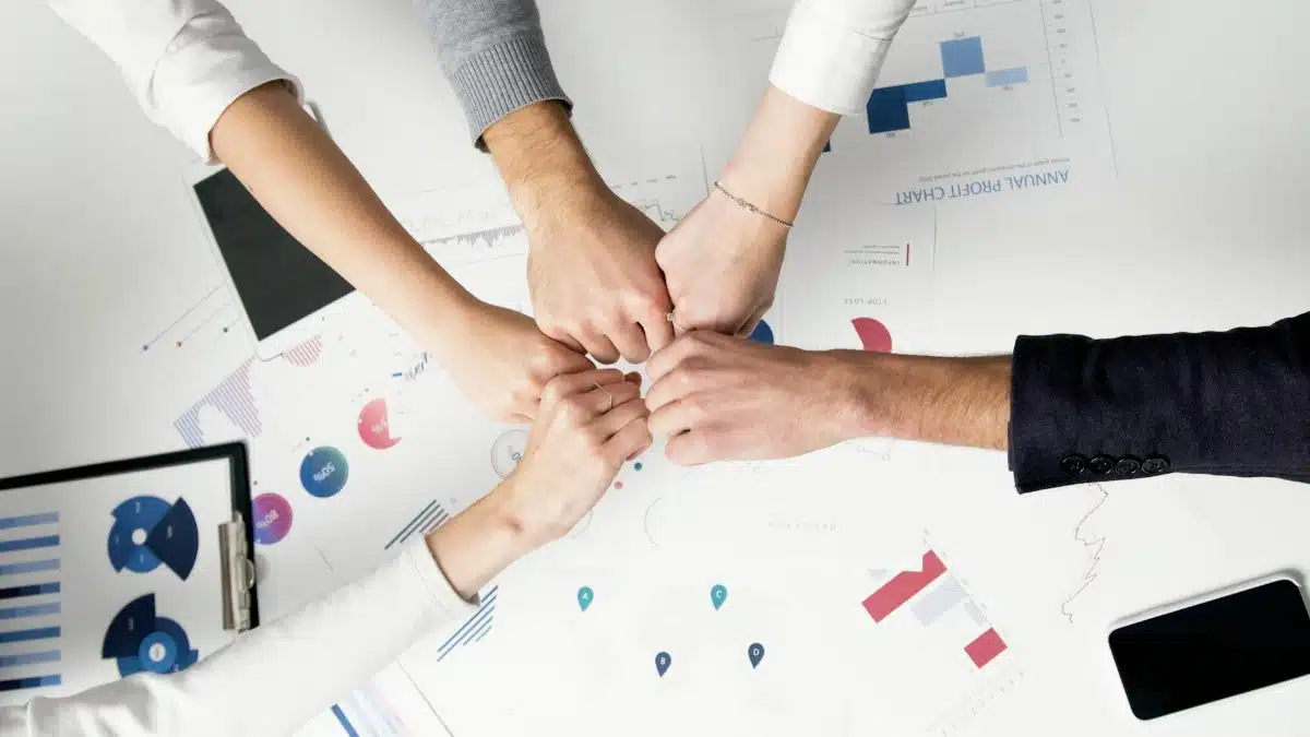 Colleagues celebrate success with a fist bump over financial charts depicting teamwork and unity.