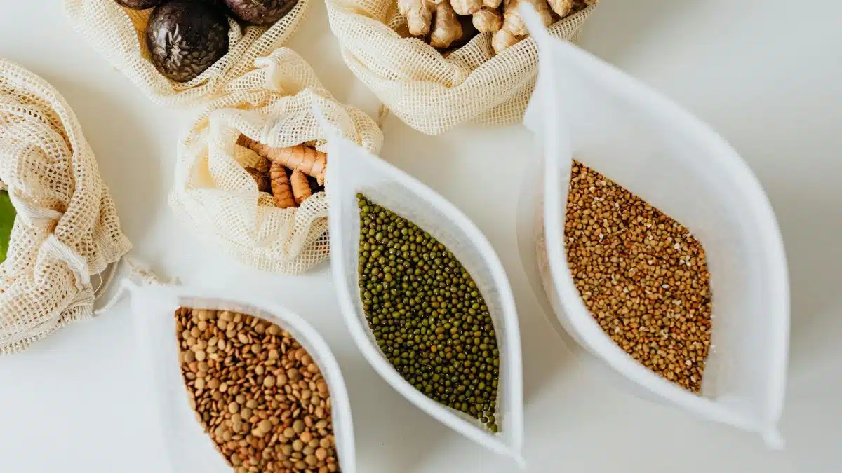 Top view of eco-friendly reusable bags with assorted grains and spices on a white surface.