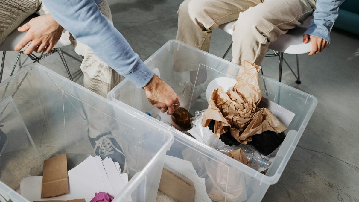 Close-up of hands sorting recyclable materials in clear plastic boxes indoors.