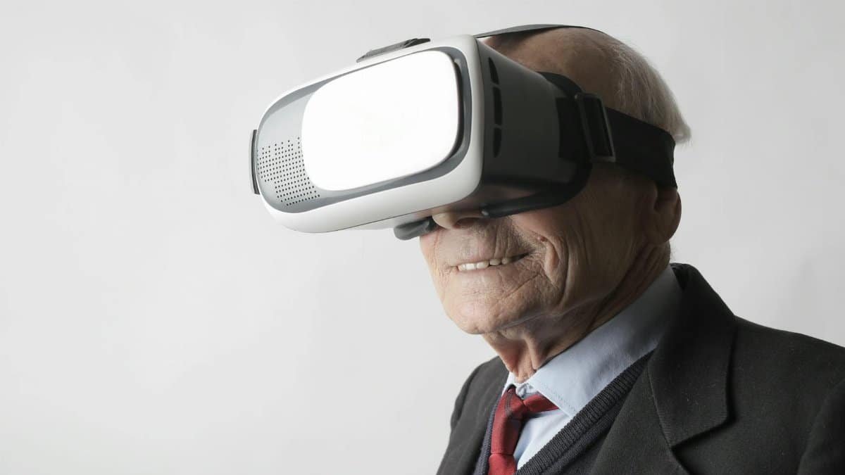 Smiling elderly gentleman wearing classy suit experiencing virtual reality while using modern headset on white background