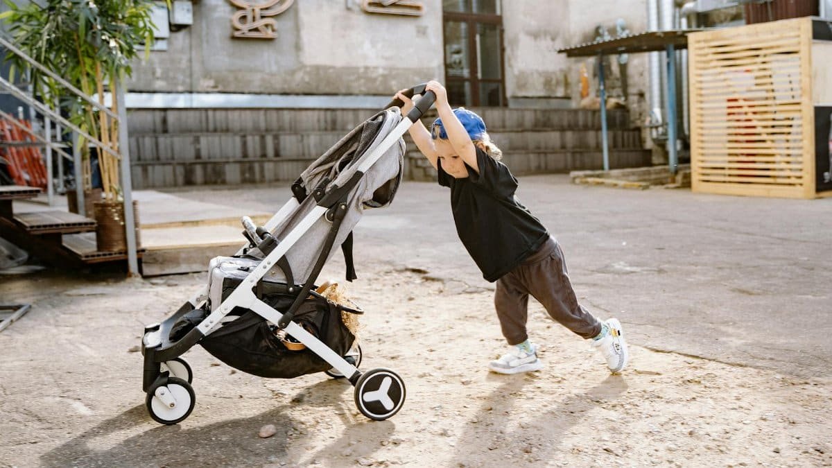 Child pushing an empty stroller in a casual urban area with industrial background.