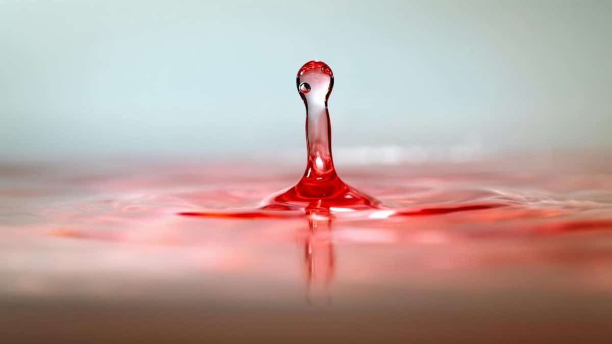 High-speed close-up of a red water droplet splash creating ripples and motion.