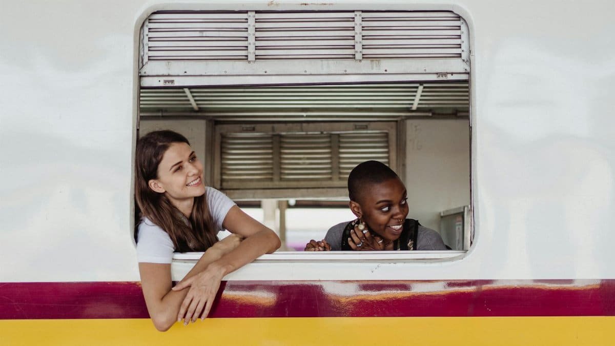 Two women looking out a train window, smiling and enjoying the journey.