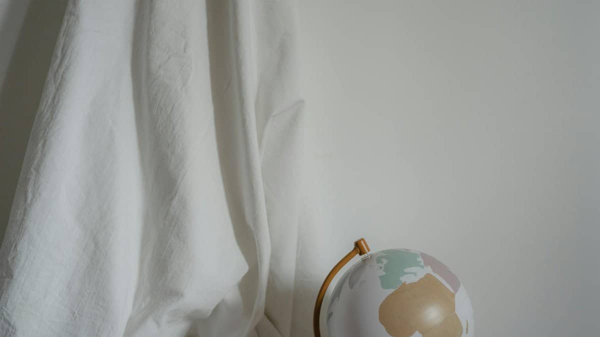 A minimalist composition of draped fabric and a globe against a white background.