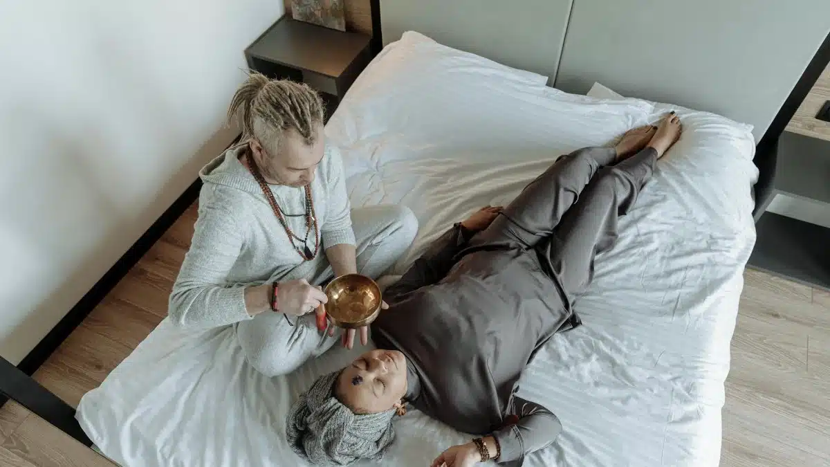 A man and woman involved in a spiritual healing session with a singing bowl on a bed.