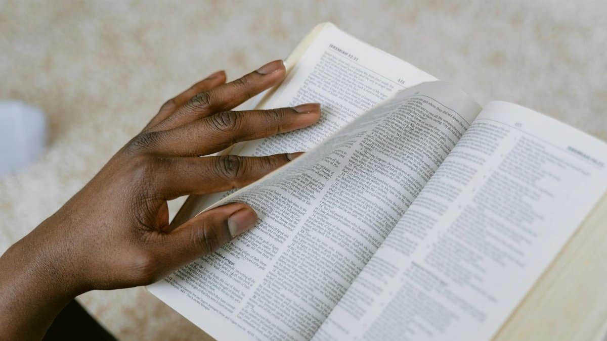 A person reads a page from the Holy Bible, focusing on scripture with a thoughtful hand turning the pages.