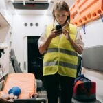 Female paramedic using smartphone inside an ambulance preparing for emergency response.