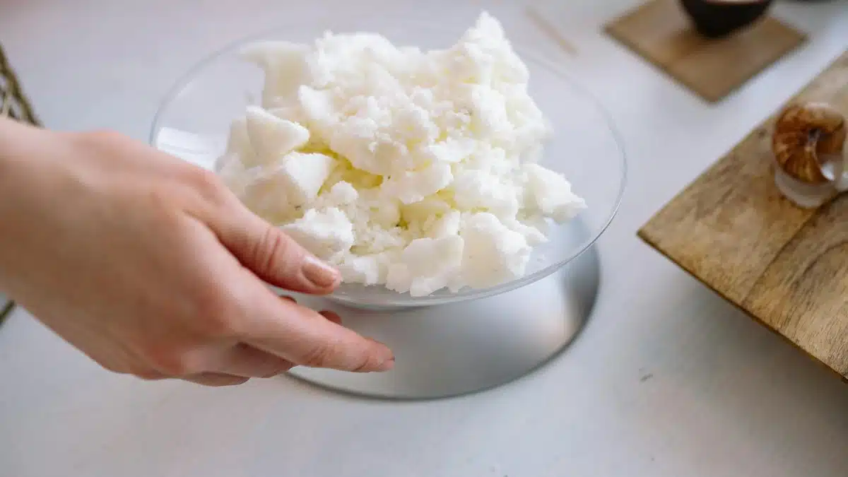 Close-up of a hand weighing candle wax indoors for crafting.