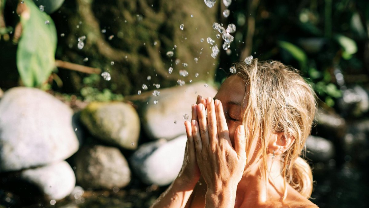 Woman enjoying a refreshing splash under natural spring water for relaxation.