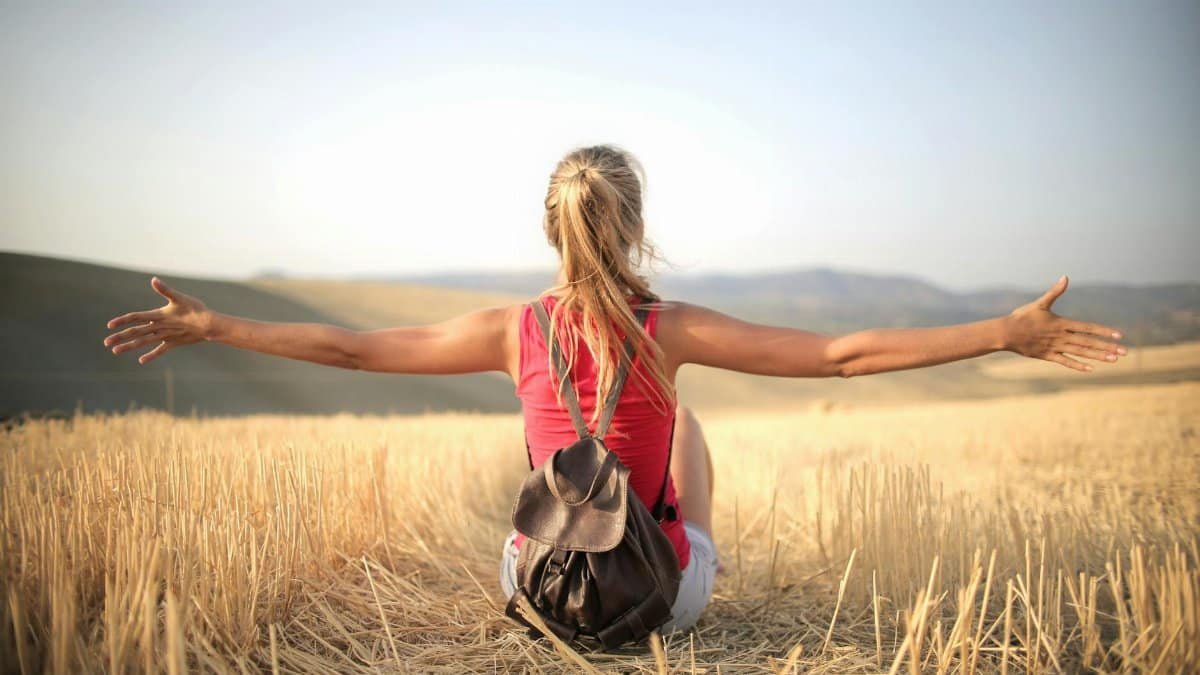 Woman enjoying the open air and freedom while sitting in a hay field during sunset.