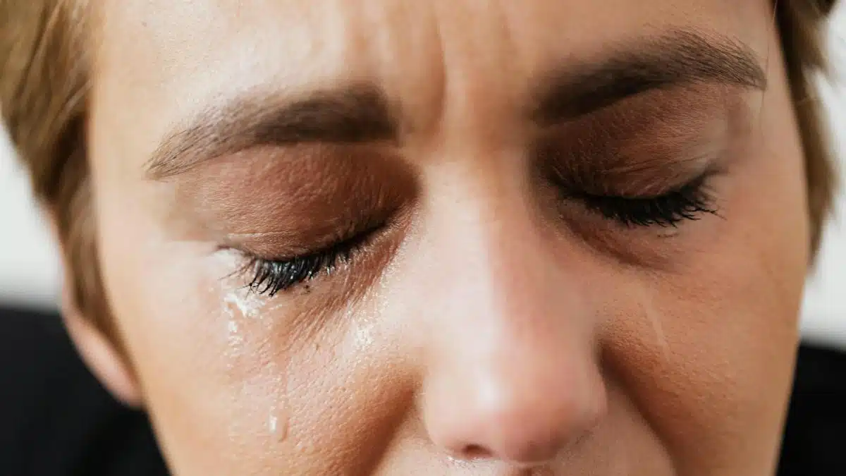 Emotional close-up of a woman's face with closed eyes and tears expressing distress.