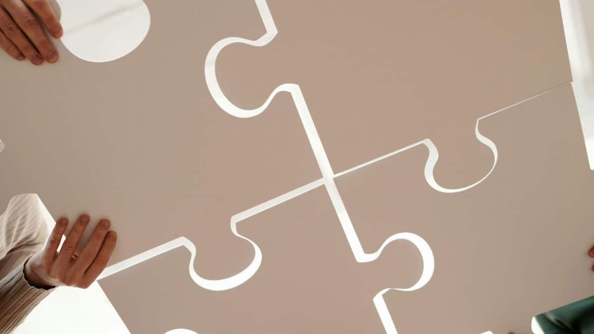 Hands of diverse individuals holding large puzzle pieces, symbolizing teamwork and unity.