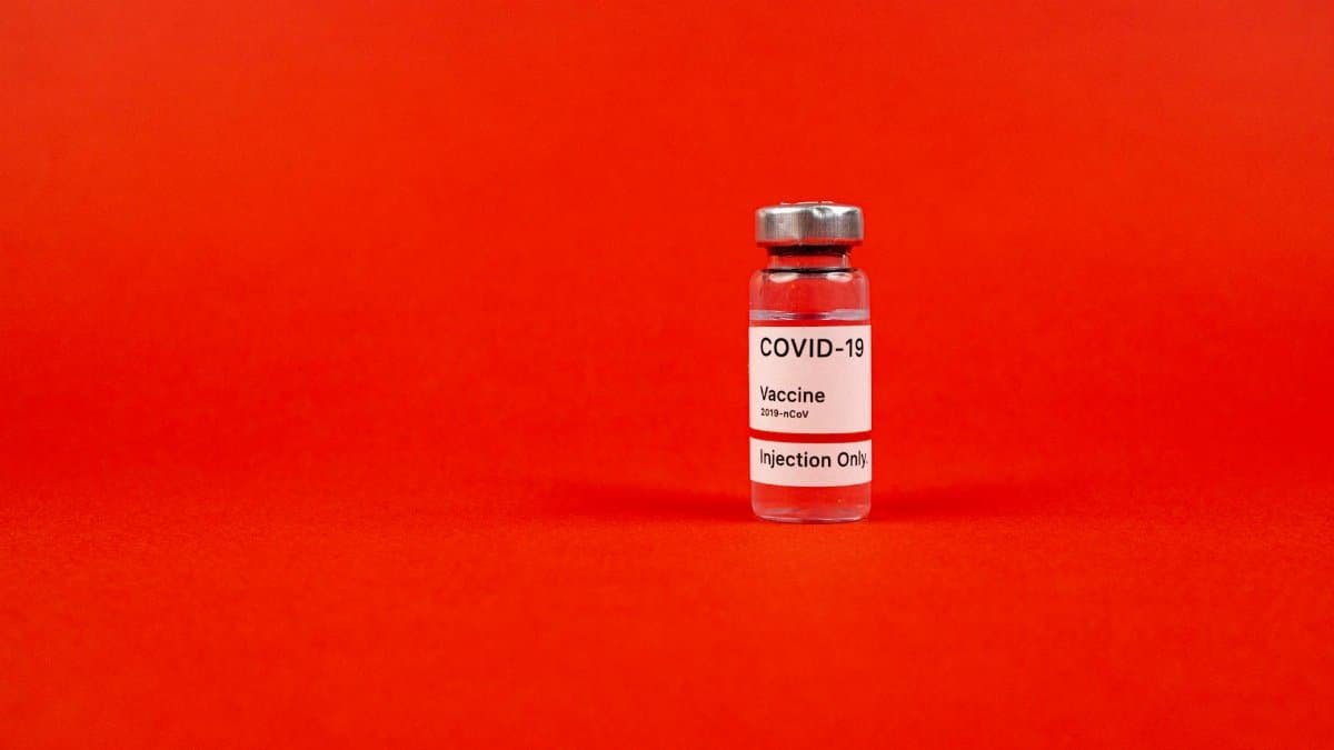 Glass vial of COVID-19 vaccine on a vibrant red backdrop, emphasizing protection.