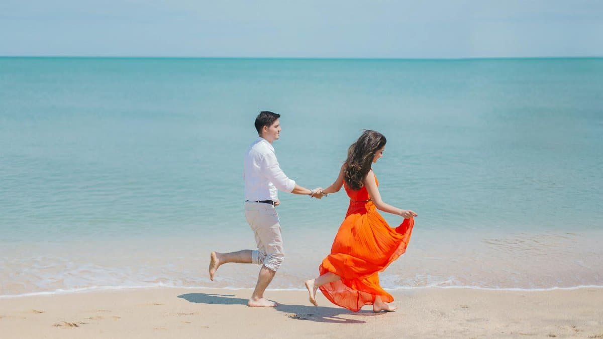 A joyful couple runs barefoot along Baku's sunny coastline, embodying carefree summer love.