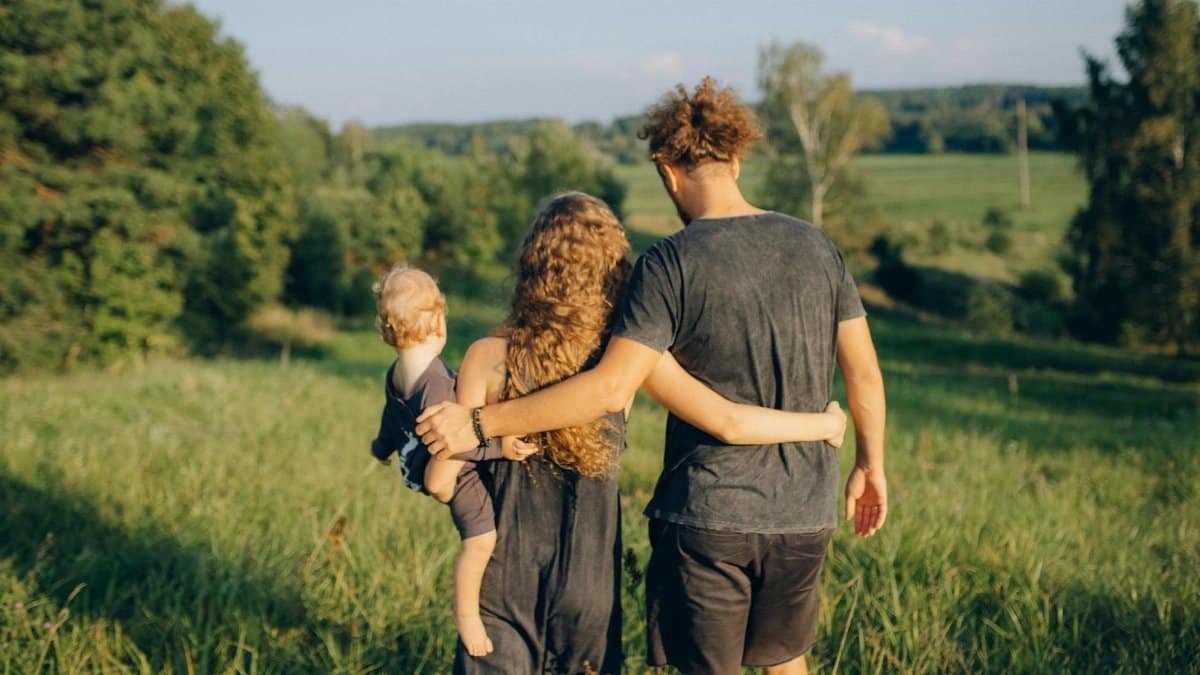 A couple with their child enjoy a serene walk through a sunlit meadow, surrounded by nature.