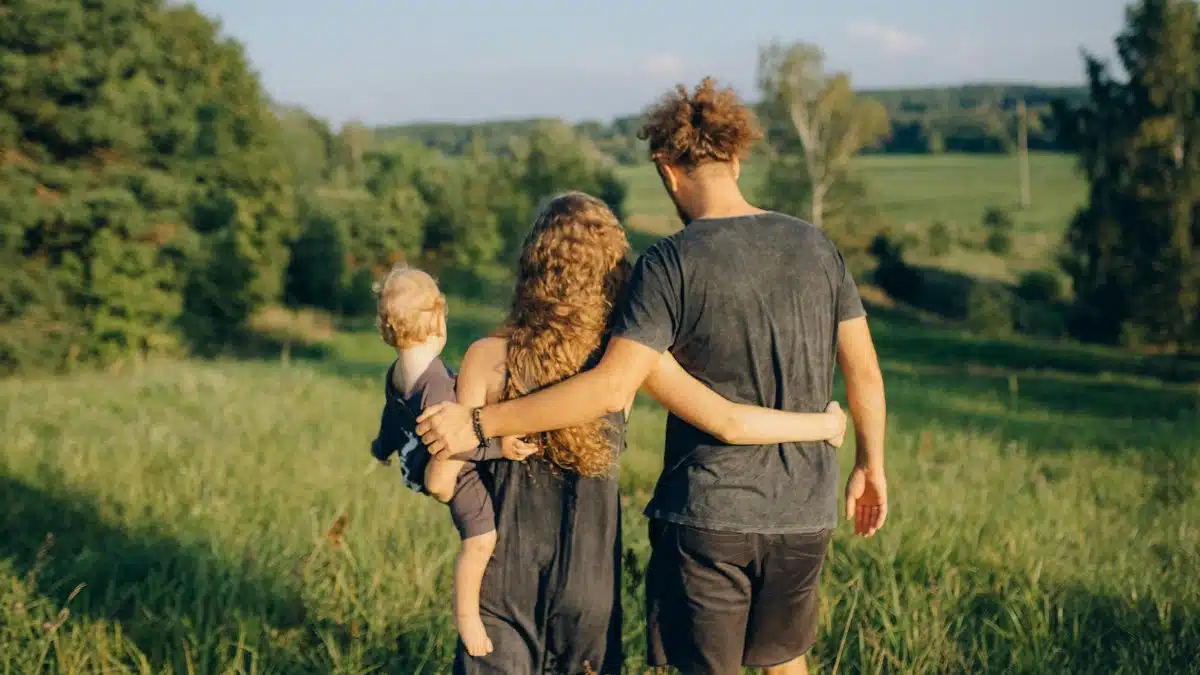 A couple with their child enjoy a serene walk through a sunlit meadow, surrounded by nature.