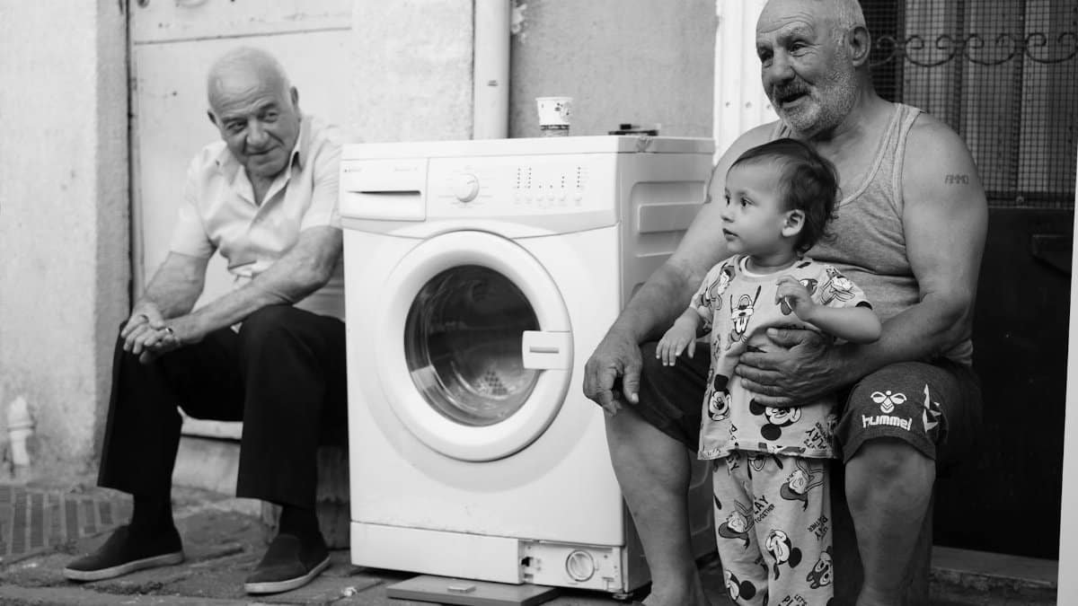 Black and white image of family members sitting outside with a washing machine.