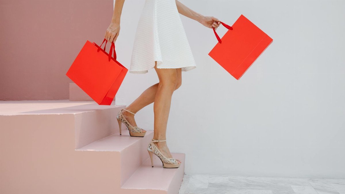 Stylish woman in high heels carrying shopping bags descends pastel pink steps.
