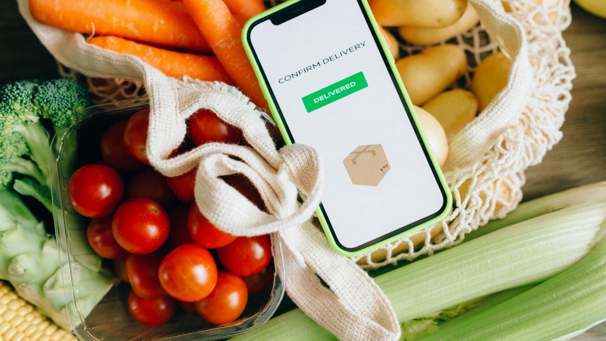 A smartphone displays delivery confirmation amidst fresh vegetables, signifying convenience and freshness.