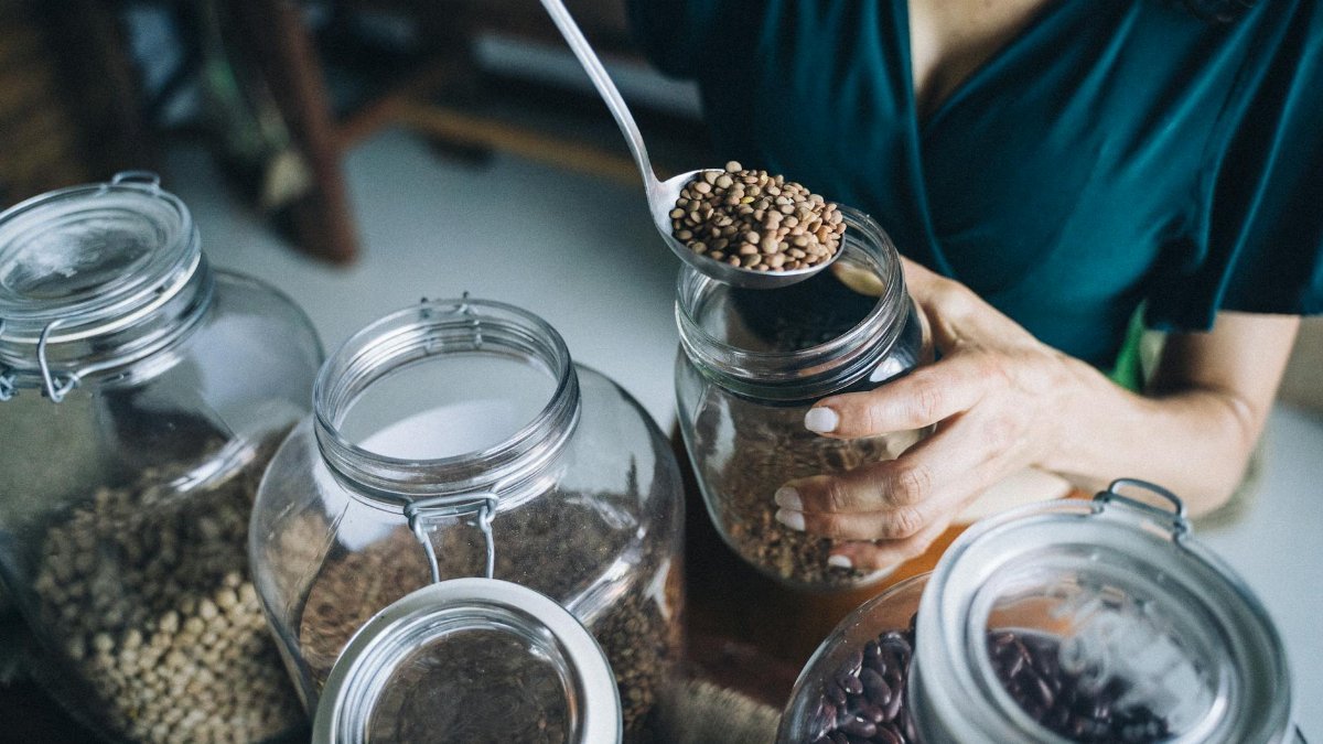 Person refilling reusable glass jars with various beans in an eco-friendly store.