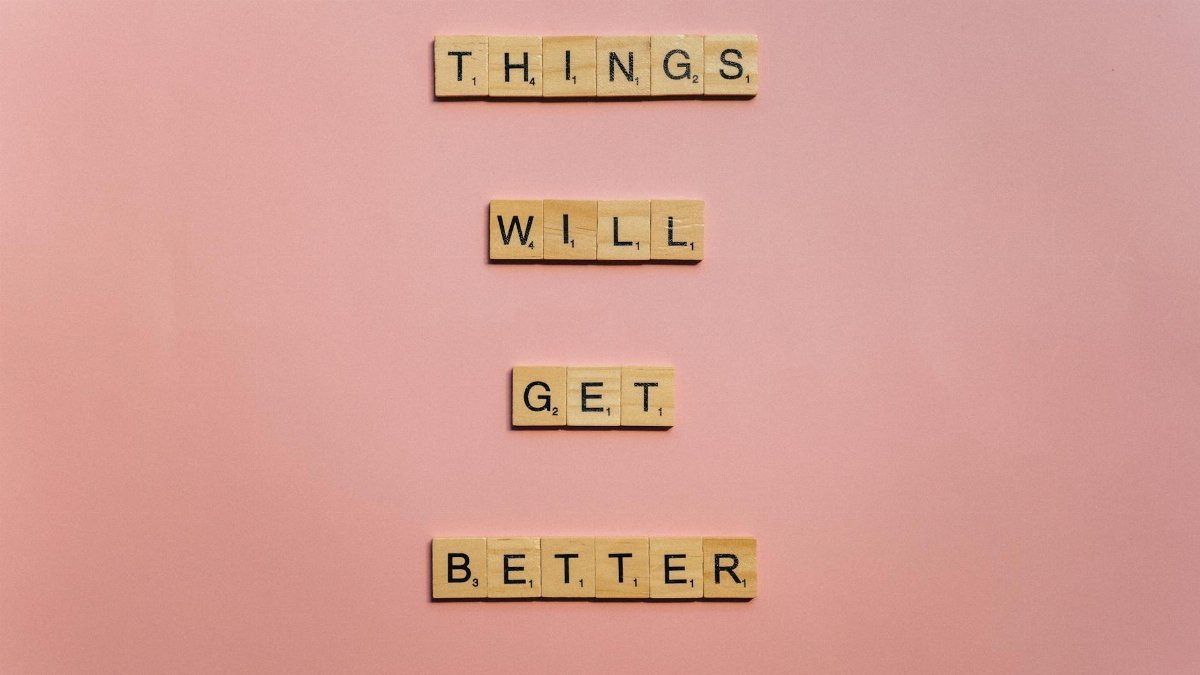 Inspirational words 'Things will get better' arranged in Scrabble tiles against a pink backdrop.