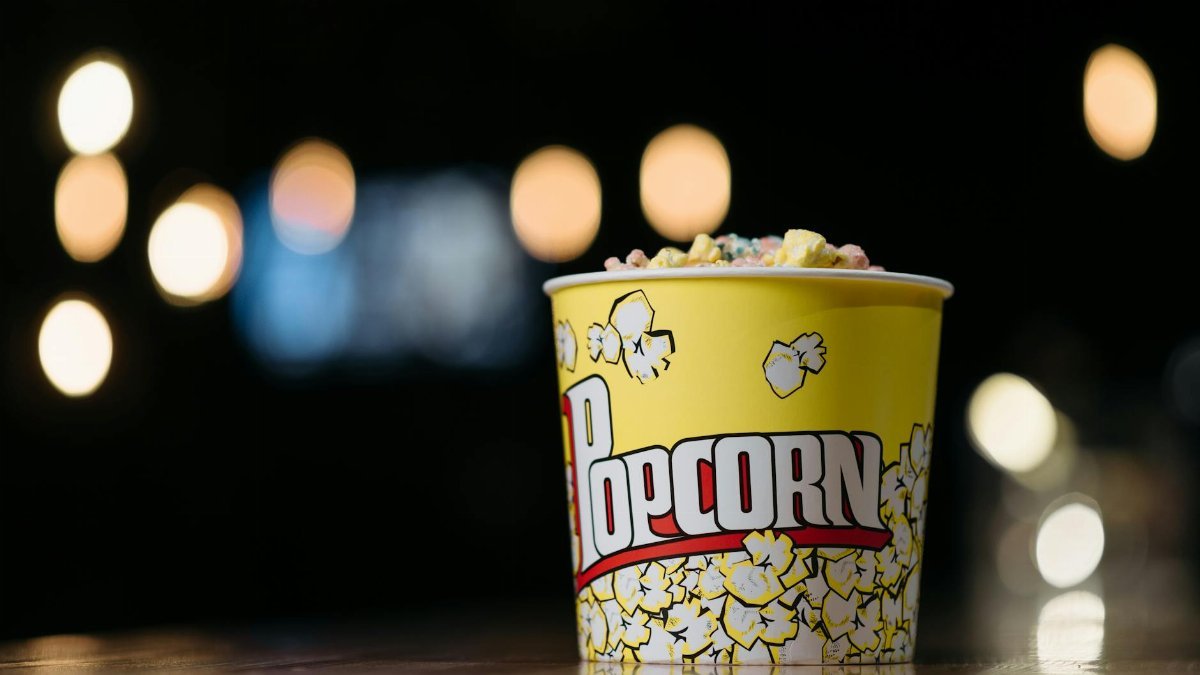 Vibrant yellow popcorn container filled with colorful popcorn against a bokeh background.