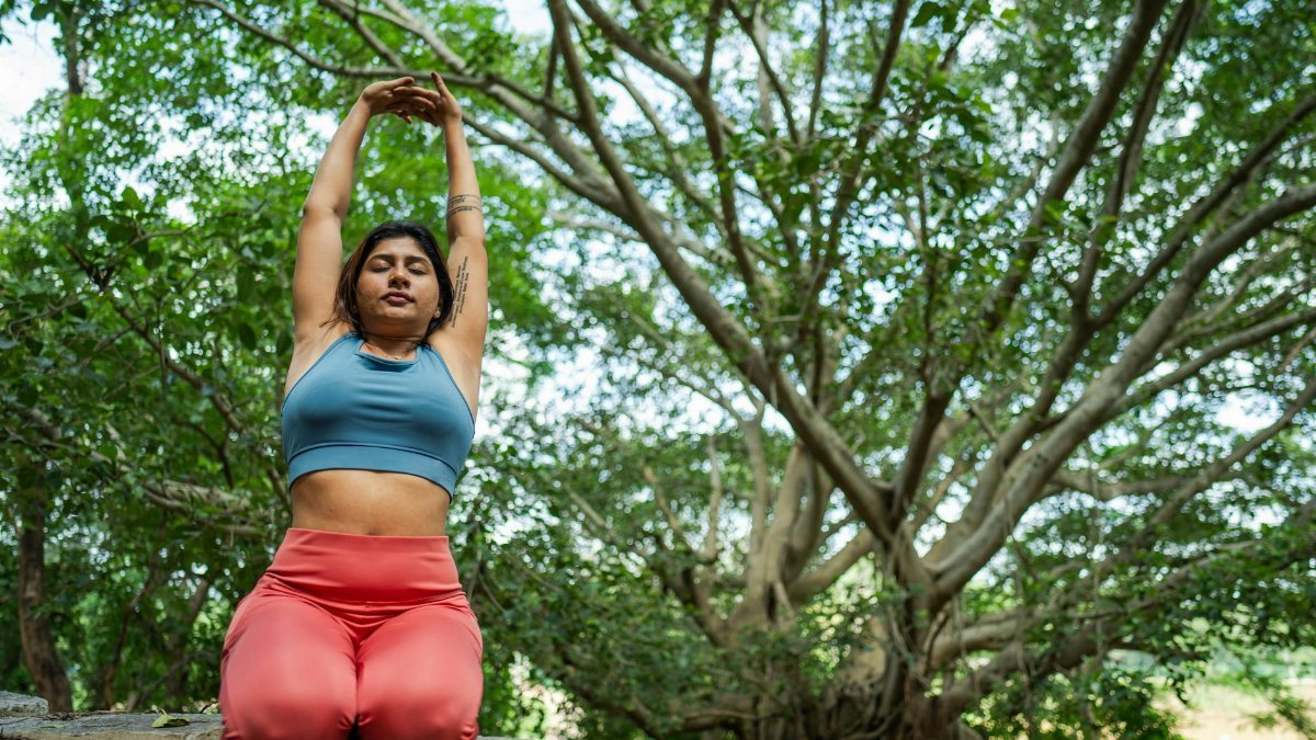 A woman practices yoga outdoors under a large tree, embracing nature and tranquility.