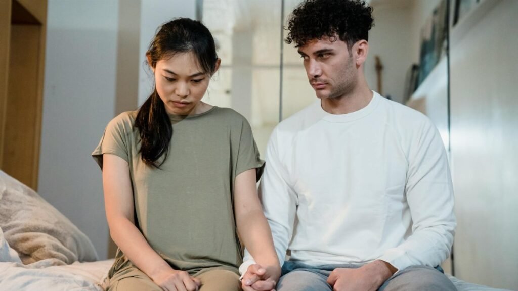 A couple sitting on a bed holding hands, facing relationship challenges indoors.